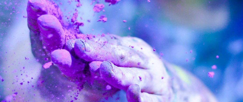 Close-up of hands throwing vibrant purple powder outdoors, capturing motion and color.